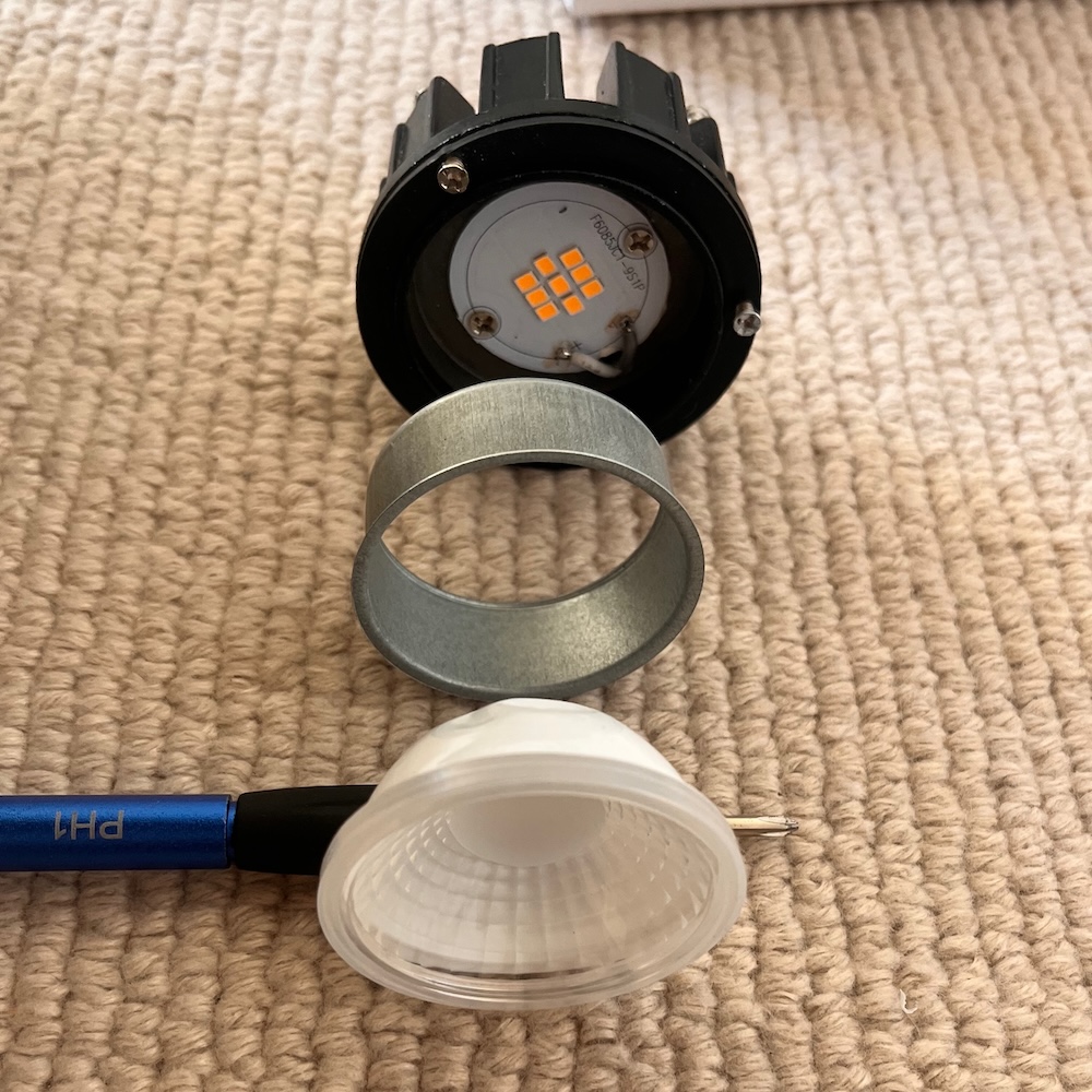 All the parts of the downlight laid out on the carpet. There's a lens, LED and various spacers.