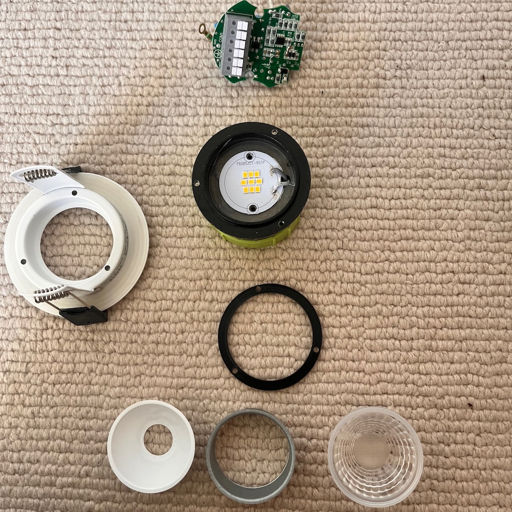 All the parts of the downlight laid out on the carpet. There's a lens, LED and various spacers.