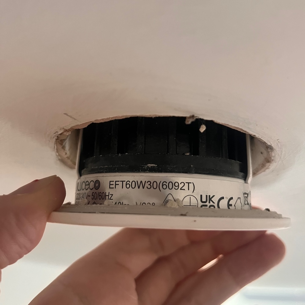 My hand pulling a circular LED downlight out of the ceiling.